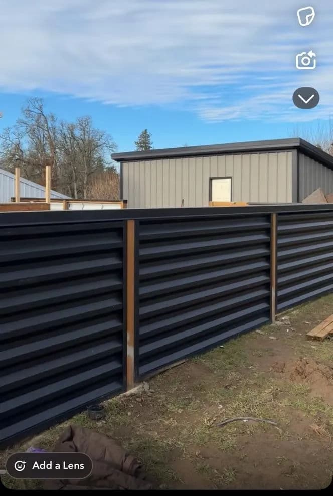 Modern corrugated metal fence with wood accents, surrounded by construction sites and trees.