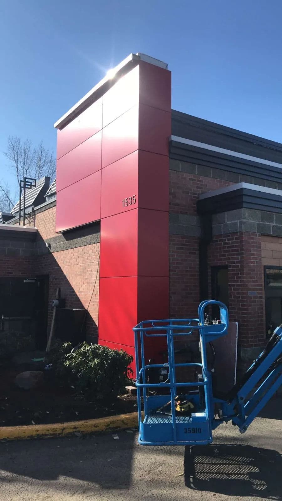 Red exterior wall of a building with construction equipment nearby and a clear blue sky.