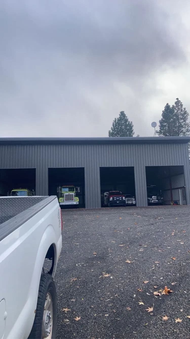 Trucks parked inside garages under cloudy sky with trees in the background.
