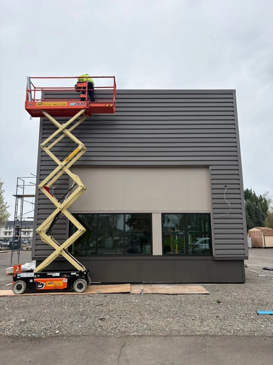 Worker on scissor lift installing exterior panels on modern commercial building façade.