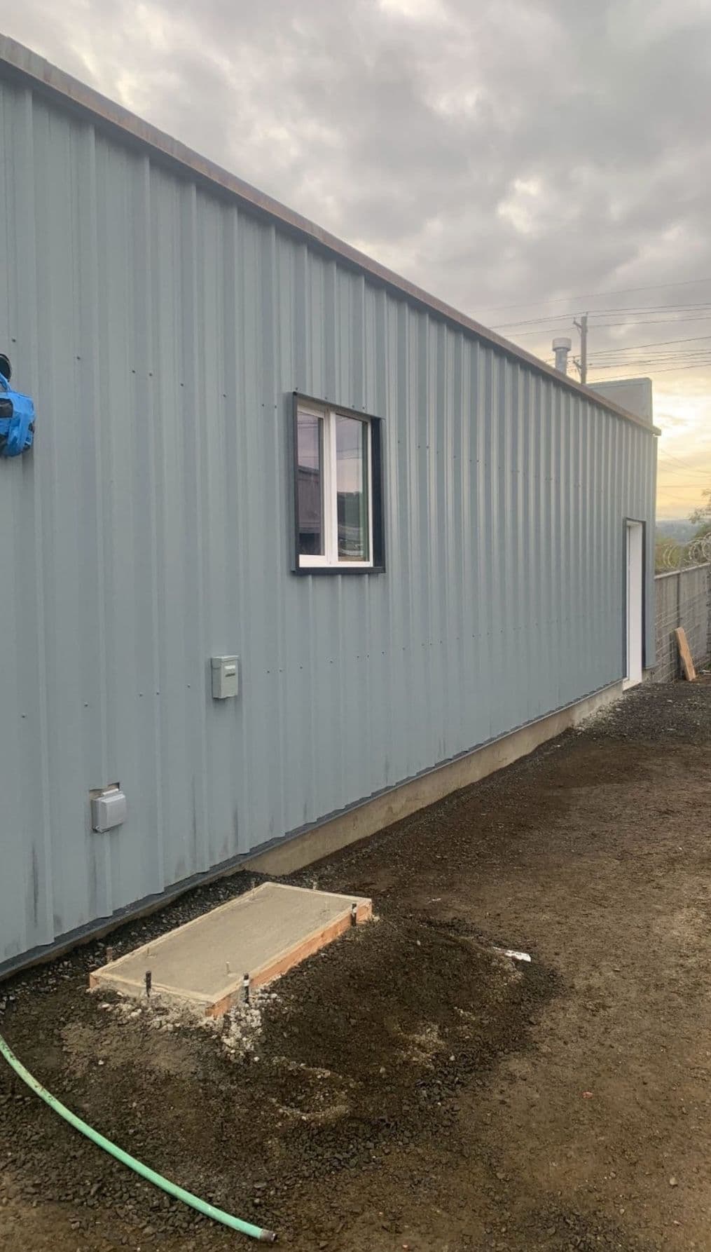 Metal building exterior with a window and concrete foundation in a construction area.