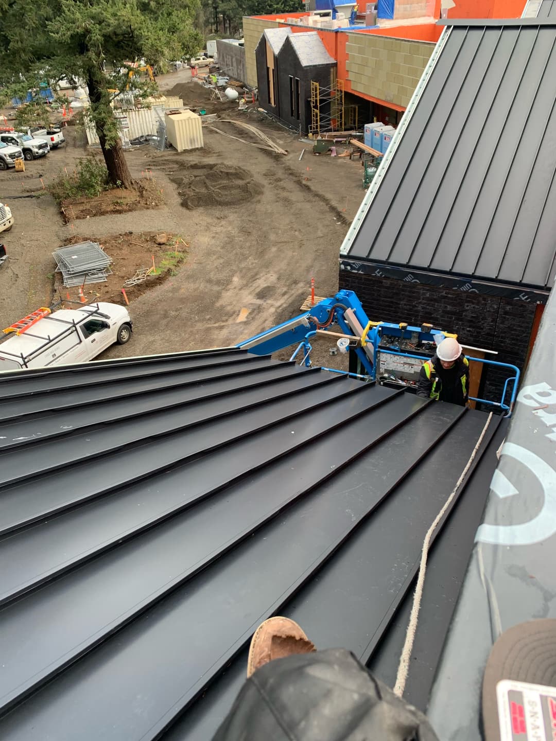 Worker on a roof using a lift for construction at a building site with machinery and materials.