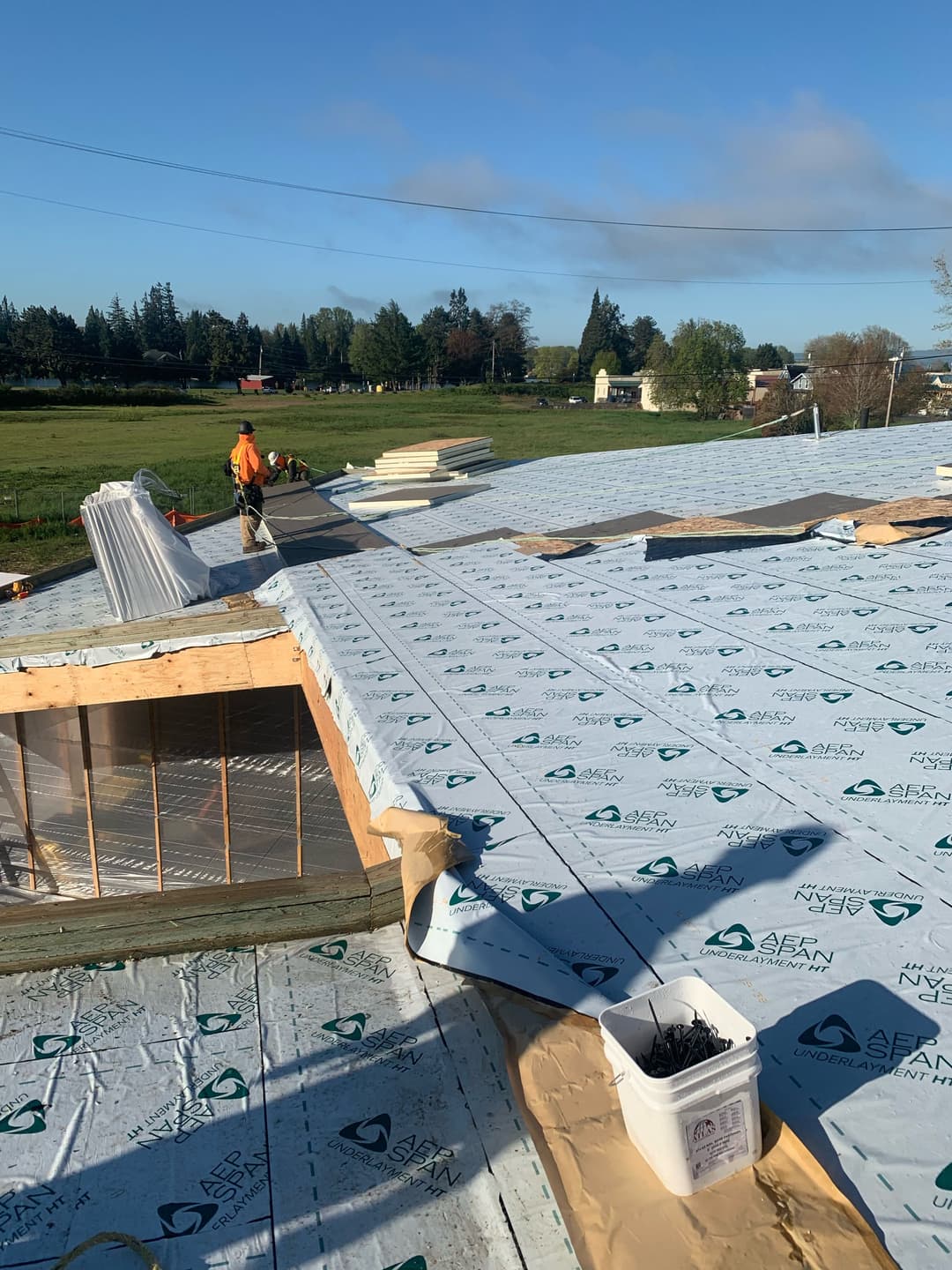 Construction worker installing roof insulation on a residential building in a rural setting.