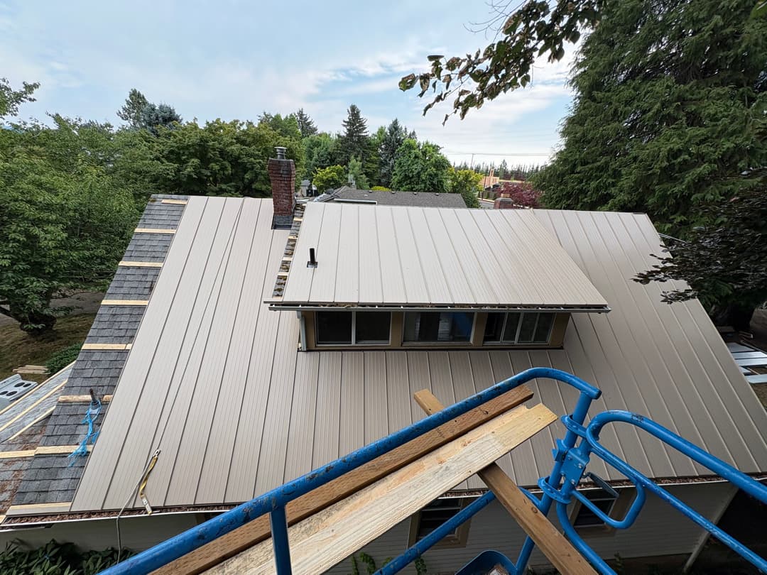 Metal roof installation on a residential home with scaffolding and trees in the background.