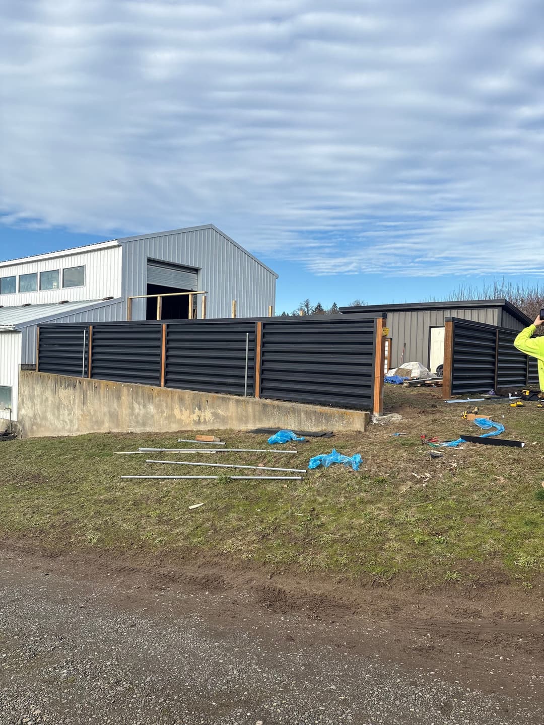 Modern black metal fence surrounding a building under construction with blue tarp elements.
