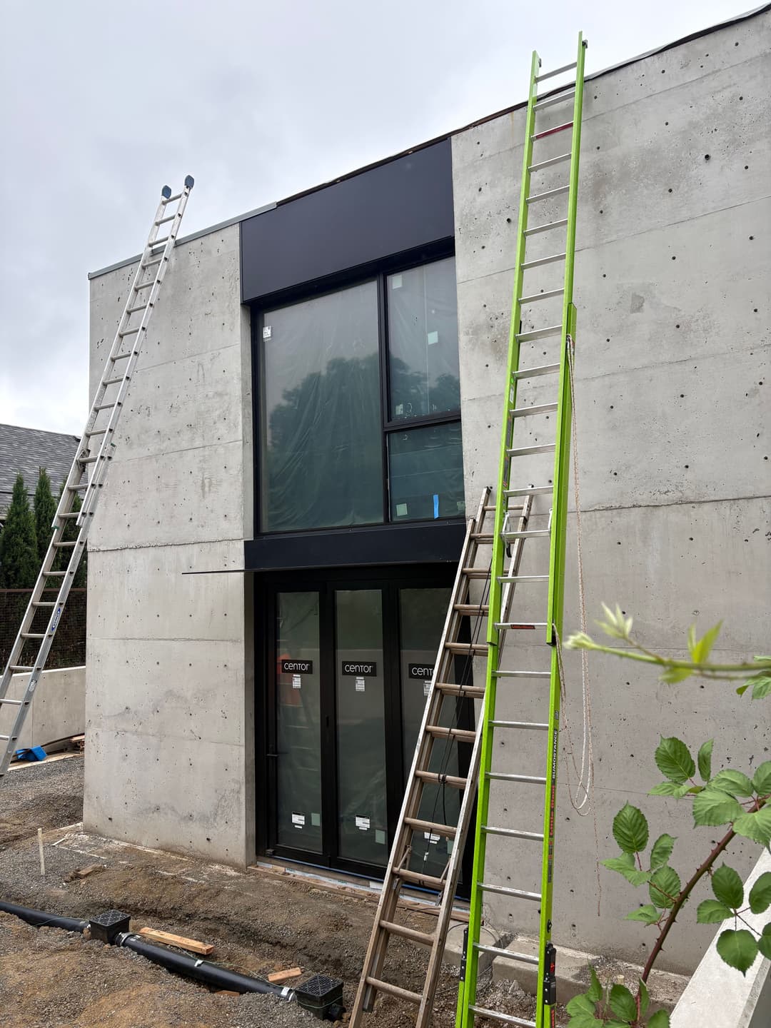 Modern building under construction with ladders and large windows on a concrete facade.