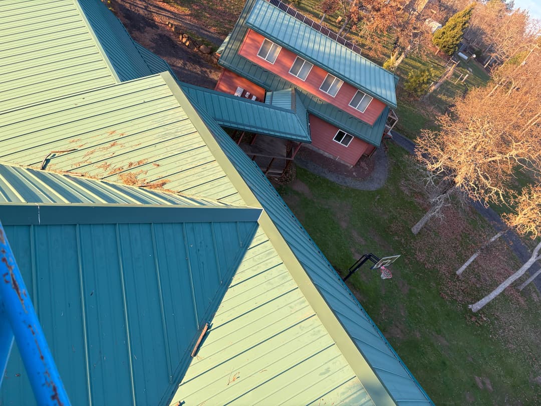 Aerial view of green metal roofs on buildings surrounded by trees and open grass.
